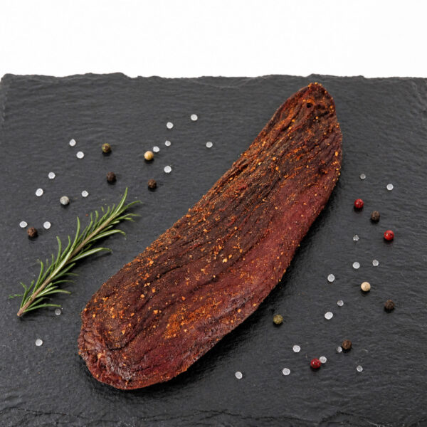 Getrocknetes, gewürztes Fleisch auf Schieferplatte – hochwertige Food‑Präsentation Ein Stück getrocknetes, gewürztes Fleisch liegt auf einer Schieferplatte, dekoriert mit grobem Salz, bunten Pfefferkörnern und einem Rosmarinzweig.
