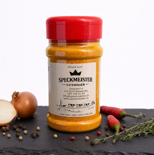 Speckmeister Luthiger Gewürzdose auf dunkler Fläche, umgeben von Zwiebeln, Chili, Pfefferkörnern und Thymian.