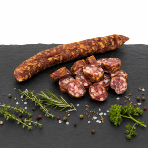 Buure Stäcke – luftgetrocknete, naturgeräucherte Schweizer Spezialität Ganze und aufgeschnittene Buure Stäcke auf dunkler Steinplatte mit Kräutern, Salz und Gewürzen