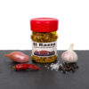 El Rasso Gewürzdose mit Chili, Knoblauch, Pfefferkörnern und Salz auf dunkler Fläche.