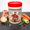 Ochsenbouillon 1 kg in Dose mit rotem Deckel, Frontansicht mit Etikette «Das Original aus der Metzgerei», auf Schieferplatte mit Markknochen, Zwiebel, Lauch, Karotten, Lorbeer, Petersilie, Pfeffer und Meersalz