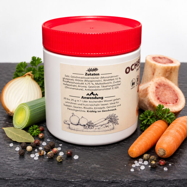 Ochsenbouillon 500 g in Dose mit rotem Deckel, linke Seite mit Zutaten und Anwendung auf der Etikette, auf Schieferplatte mit Markknochen, Zwiebel, Lauch, Karotten, Lorbeer, Petersilie, Pfeffer und Meersalz