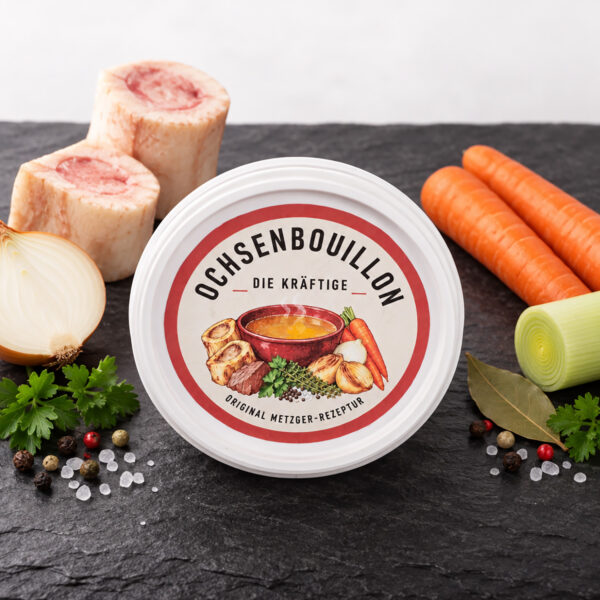Ochsenbouillon 150 g von oben, Deckeletikette «Die Kräftige - Original Metzger-Rezeptur», auf Schieferplatte mit Markknochen, Zwiebel, Lauch, Karotten, Lorbeer, Petersilie, Pfeffer und Meersalz